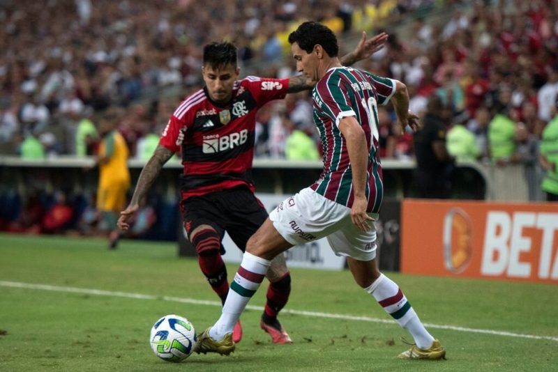 Ilustrando a Qual a maior rivalidade do futebol brasileiro: Dois jogadores de futebol, um do flamengo (com uniforme vermelho e preto, em listras horizontais) e um do fluminense (uniforme bordô, verde e branco, em listras verticais) disputando a bola em campo.